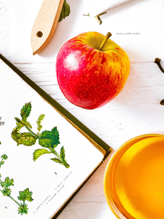 Apple and apple tea next to a botanical book.